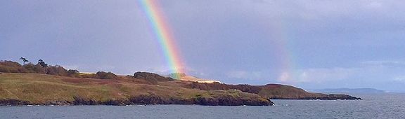 The edges of a rainbow meet the edges of San Juan Island. Photo by Alex Shapiro.